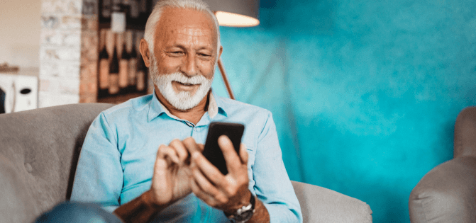 Elderly man with a white beard smiling while using a smartphone
